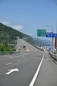 An empty highway with directional signs and lush mountains in the background.