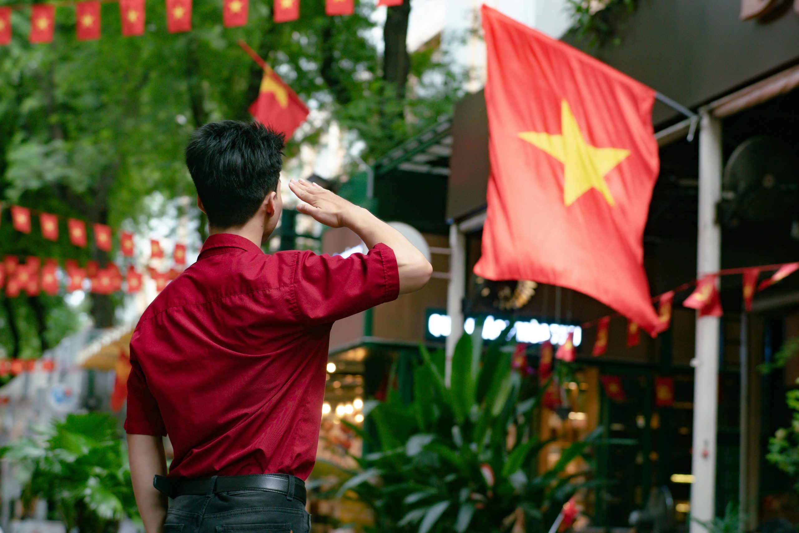 A man in red saluting the Vietnamese flag on a vibrant street in Ho Chi Minh City.